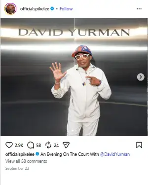 Spike Lee posing in an all-white tracksuit and colorful cap with an open palm gesture in front of a David Yurman backdrop.