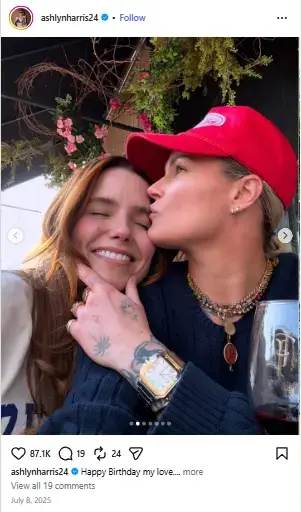 Ashlyn Harris in a red cap kissing a smiling Sophia Bush on the cheek while resting her chin in her tattooed hand.