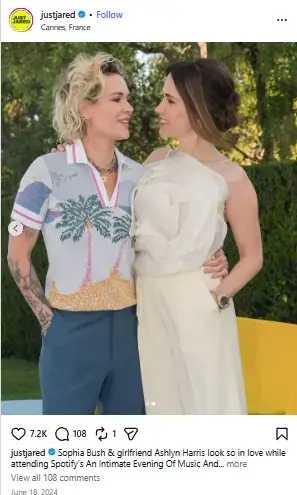 Ashlyn Harris in a palm tree knit polo embracing and gazing into the eyes of Sophia Bush in an elegant white ruffled ensemble outdoors.