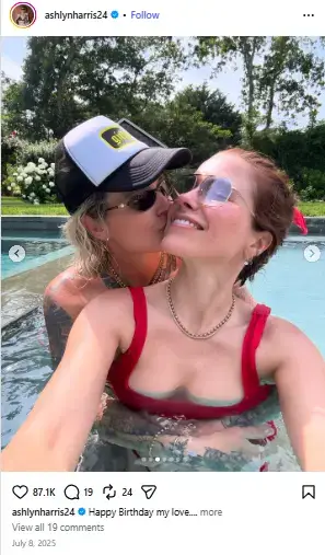 Ashlyn Harris wearing a trucker hat kisses Sophia Bush on the cheek as they relax together in a swimming pool.
