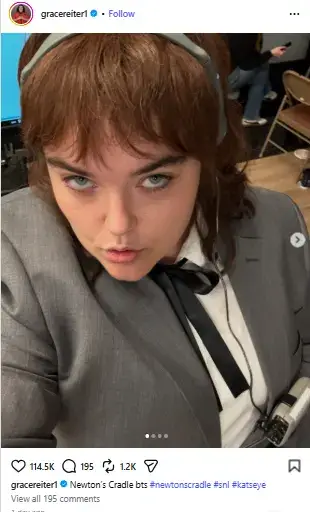 Grace Reiter leaning forward into a high-angle selfie wearing a grey blazer, black necktie, and headset headphones.