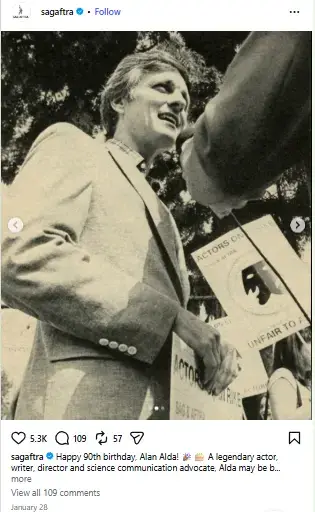 Alan Alda smiling and holding a strike picket sign while speaking to a reporter at an actors