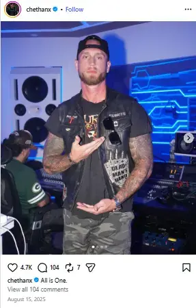 Chet Hanks standing inside a neon-lit music recording studio wearing a backwards cap, a biker vest, and camouflage pants.