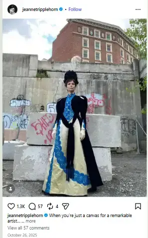 Jeanne Tripplehorn posing in an elaborate period costume gown, dark velvet cape, and headpiece against an urban concrete backdrop.