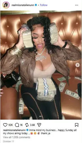 Natalie Nunn holding thick stacks of cash to her ears while sitting on a leather booth with banded money bundles in her lap.