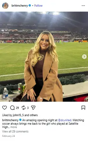 Britt McHenry smiling pitchside in a camel coat and turtleneck against a soccer stadium backdrop.
