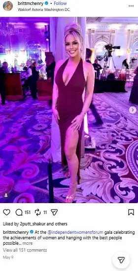 Britt McHenry posing in a floor-length burgundy gown with a thigh-high slit and plunging neckline in a ballroom.