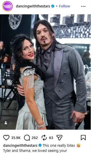Sharna Burgess in a vintage embellished dress posing beside Tyler Cameron wearing a dark tuxedo, long wig, and vampire goatee backstage.