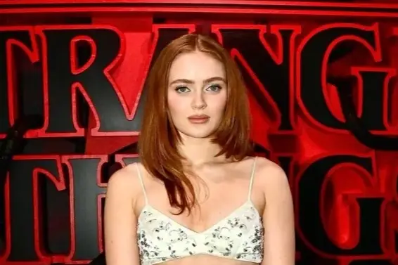 Actress Sadie Sink posing in a white two-piece embellished gown in front of a red Stranger Things ba
