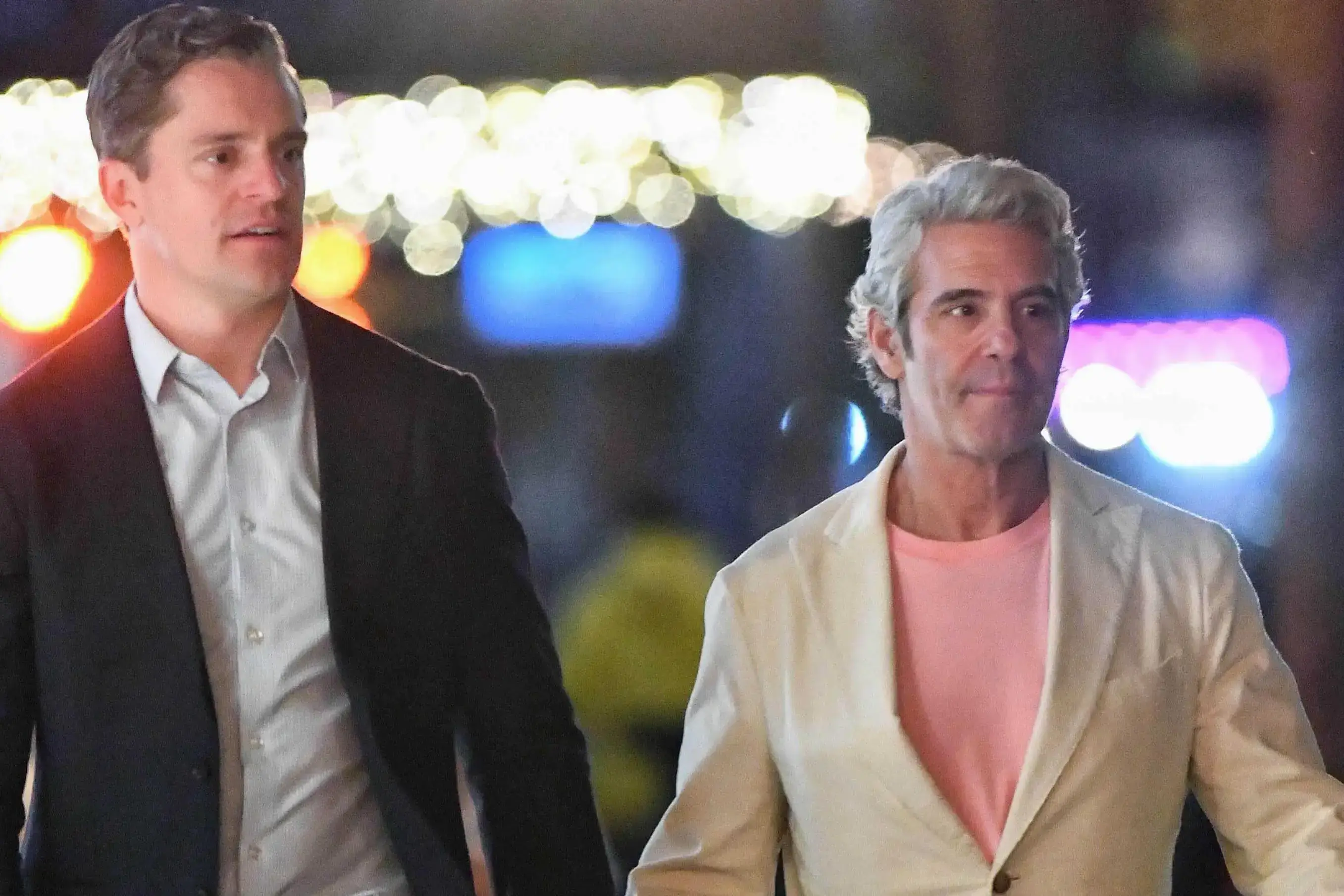 Kevin Sobieski in a dark suit walking alongside Andy Cohen, who is wearing a cream jacket over a pin