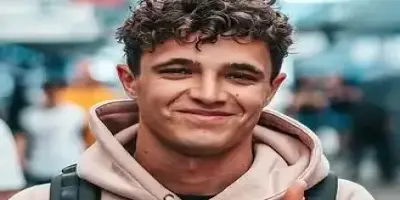 A close-up portrait of Lando Norris smiling and wearing a light brown hoodie.