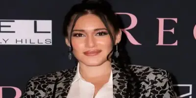 Q'orianka Kilcher smiling and wearing a patterned blazer and a white shirt.
