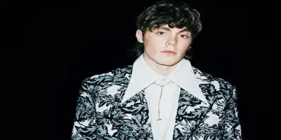 Jack Champion poses wearing a dark, textured blazer over a white shirt.