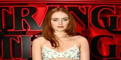 Actress Sadie Sink posing in a white two-piece embellished gown in front of a red Stranger Things ba