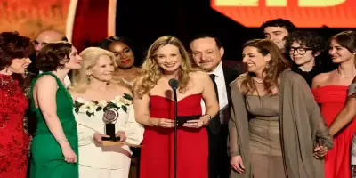 Bess Wohl in a red dress smiles at a microphone on stage surrounded by artists at an Tony awards cer